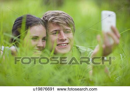Stock Image - Young couple self-photographing on grass. Fotosearch