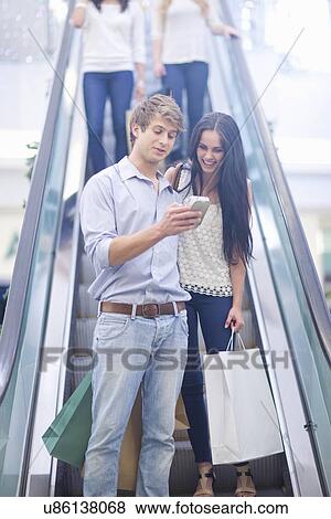 Young couple using cellular phone on escalator View Large Photo Image Stock Photo - Young couple using cellular phone on escalator. Fotosearch