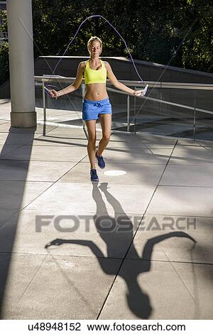 Stock Image - Young female athlete skipping in urban sunlight. Fotosearch