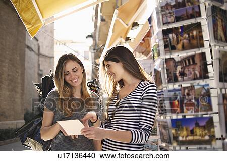 Stock Image - Young female friends looking at postcards, Valencia, Spain. Fotosearch