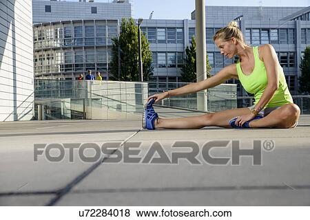 Stock Photo - Young female runner stretching on city rooftop. Fotosearch