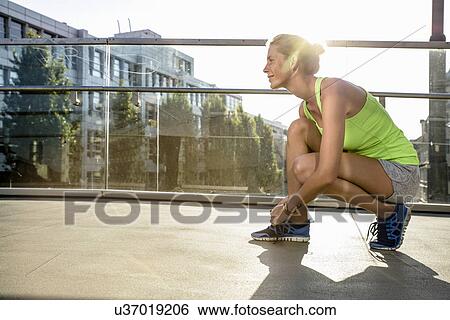 Young female runner tying shoelace on city footbridge View Large Photo Image Stock Photograph - Young female runner tying shoelace on city footbridge. Fotosearch