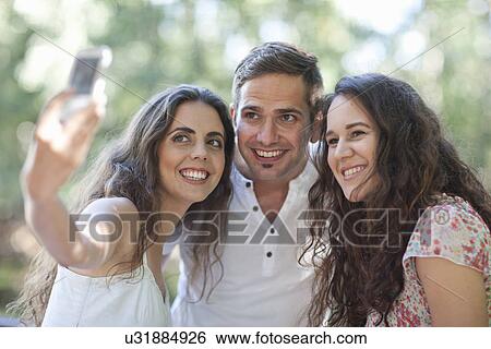Young friends taking a self portrait on camera phone View Large Photo Image Stock Photograph - Young friends taking a self portrait on camera phone. Fotosearch