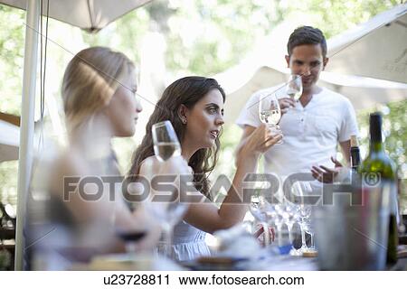 Stock Image - Young friends tasting and looking at wine at vineyard bar. Fotosearch