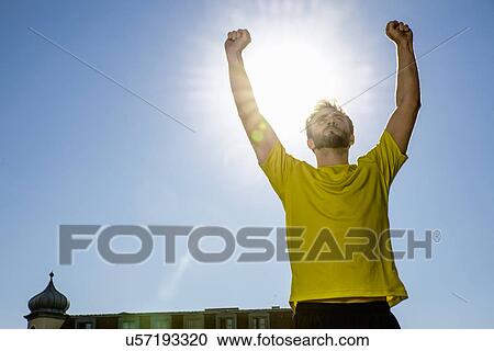 Stock Image - Young male athlete celebrating on city rooftop. Fotosearch