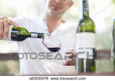 Stock Photograph - Young male waiter pouring red wine at vineyard bar. Fotosearch