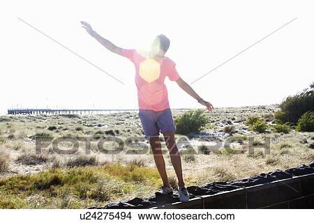 Young man balancing on wall near coast, Port Melbourne, Melbourne, Australia View Large Photo Image Picture - Young man balancing on wall near coast, Port Melbourne, Melbourne, Australia. Fotosearch