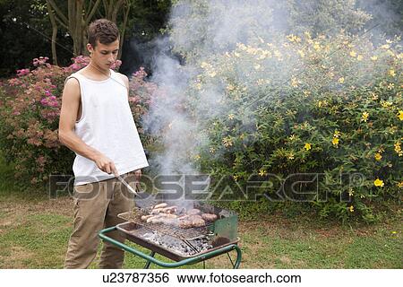 Young man barbecuing meat in garden View Large Photo Image Stock Photograph - Young man barbecuing meat in garden. Fotosearch