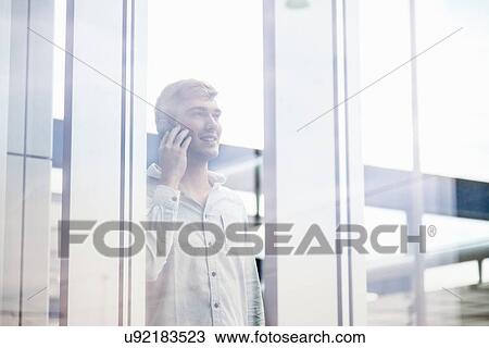 Young man behind reflective glass talking on smartphone View Large Photo Image Stock Image - Young man behind reflective glass talking on smartphone. Fotosearch