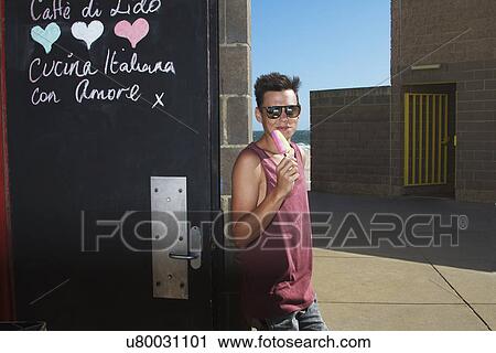 Young man enjoying ice lolly outside ice cream parlour View Large Photo Image Stock Image - Young man enjoying ice lolly outside ice cream parlour. Fotosearch