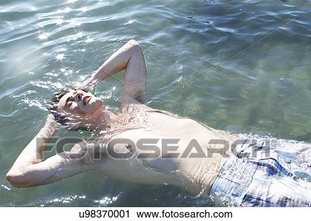 Young man floating in water with hands behind head View Large Photo Image Stock Image - Young man floating in water with hands behind head. Fotosearch