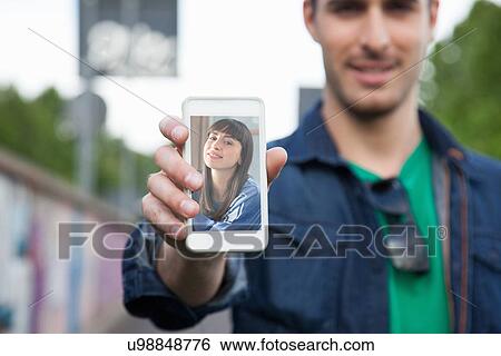 Young man holding up smartphone with photograph of girlfriend View Large Photo Image Stock Photograph - Young man holding up smartphone with photograph of girlfriend. Fotosearch