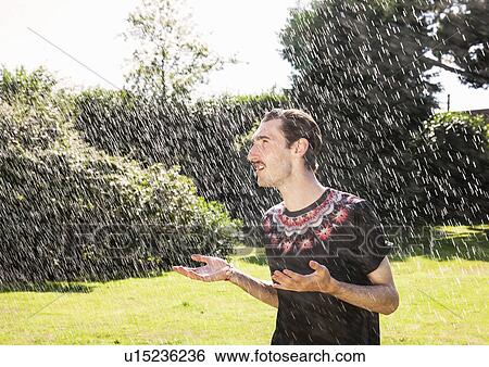 Stock Photograph - Young man in garden sprinkler. Fotosearch