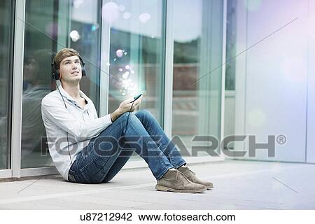 Stock Image - Young man in headphones with lights coming out of smartphone. Fotosearch