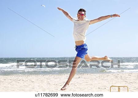 Stock Photo - Young man leaping mid air on beach, Port Melbourne, Melbourne, Australia. Fotosearch