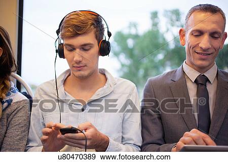 Young man listening to headphones and using smartphone on train View Large Photo Image Stock Photo - Young man listening to headphones and using smartphone on train. Fotosearch
