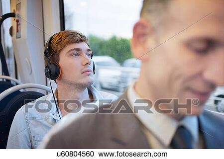 Stock Image - Young man listening to headphones on train. Fotosearch