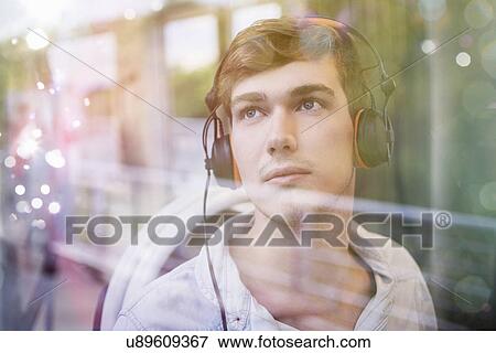 Stock Photo - Young man on train, daydreaming and listening to headphones. Fotosearch