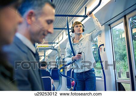 Stock Image - Young man on train listening to headphones. Fotosearch