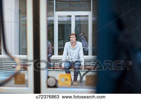 Stock Image - Young man sitting on train station bench. Fotosearch