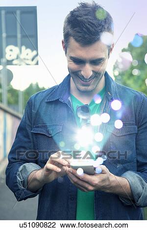 Young man texting on smartphone with glowing lights coming out of it View Large Photo Image Stock Image - Young man texting on smartphone with glowing lights coming out of it. Fotosearch