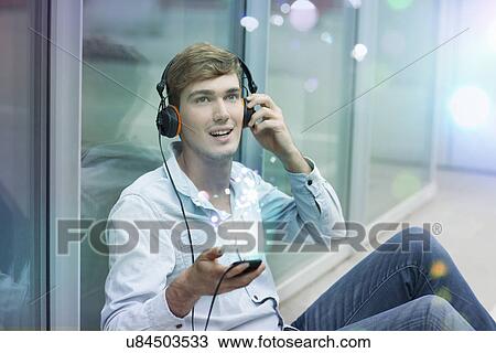 Stock Image - Young man with headphones and smartphone with lights coming out of it. Fotosearch