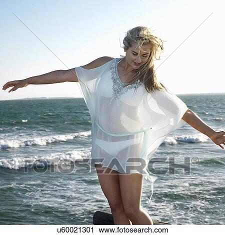 Young woman balancing with arms outstretched at coast View Large Photo Image Stock Image - Young woman balancing with arms outstretched at coast. Fotosearch