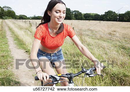 Young woman cycling on dirt track in field View Large Photo Image Stock Image - Young woman cycling on dirt track in field. Fotosearch