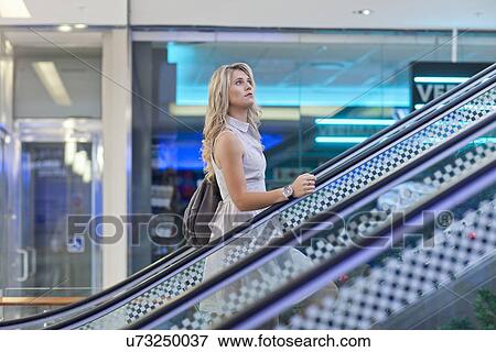 Young woman going up escalator in mall View Large Photo Image Stock Photo - Young woman going up escalator in mall. Fotosearch