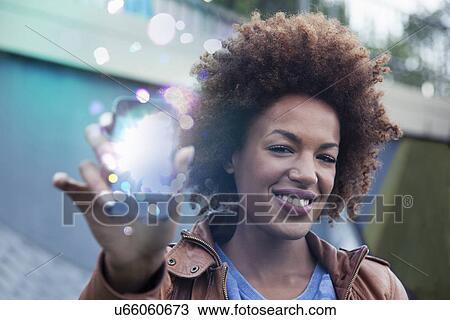 Young woman holding up smartphone with glowing lights coming out View Large Photo Image Stock Image - Young woman holding up smartphone with glowing lights coming out. Fotosearch