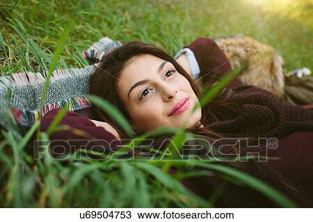 Stock Image - Young woman lying on blanket on grass. Fotosearch