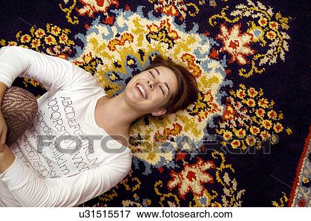 Stock Photo - Young woman lying on patterned rug laughing. Fotosearch