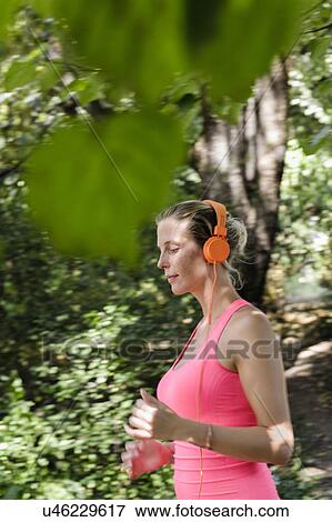 Stock Photo - Young woman running through wooded park. Fotosearch
