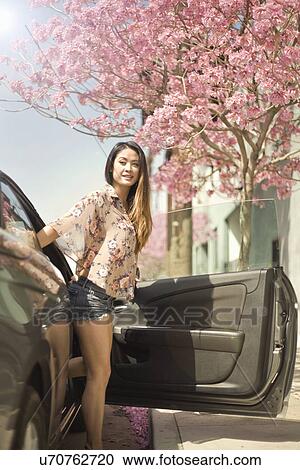 Stock Image - Young woman stepping out of car door. Fotosearch