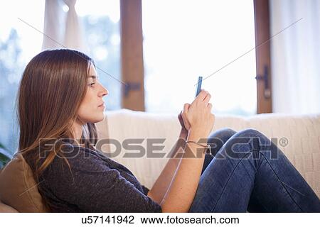 Young woman using cellular phone on sofa View Large Photo Image Stock Image - Young woman using cellular phone on sofa. Fotosearch