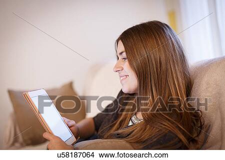 Picture - Young woman using digital tablet on sofa. Fotosearch
