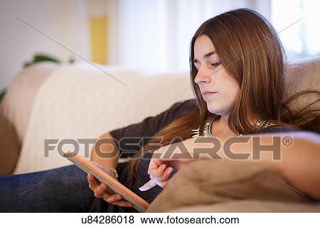 Stock Photo - Young woman using digital tablet on sofa. Fotosearch