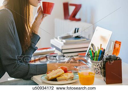 Young woman using laptop while breakfasting View Large Photo Image Stock Image - Young woman using laptop while breakfasting. Fotosearch