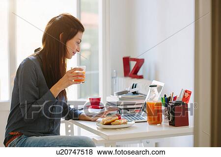 Young woman using laptop while breakfasting View Large Photo Image Stock Photo - Young woman using laptop while breakfasting. Fotosearch