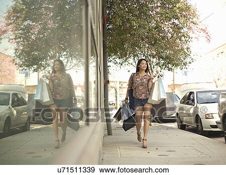 Young woman walking down street with shopping bags View Large Photo Image Stock Photo - Young woman walking down street with shopping bags. Fotosearch