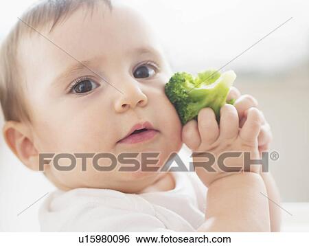 Stock Photograph - Baby girl (12-17 months) holding broccoli. Fotosearch