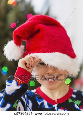 Stock Image - Boy (6-7) peeking through santa hat. Fotosearch