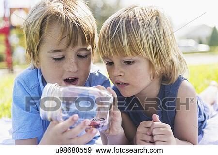 Stock Photo - Boys (4-5, 8-9) watching butterfly in jar. Fotosearch