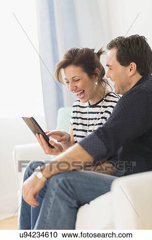 Couple sitting on sofa looking at digital tablet View Large Photo Image Stock Image - Couple sitting on sofa looking at digital tablet. Fotosearch