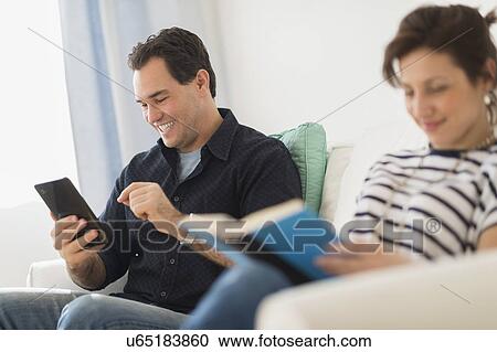 Couple sitting on sofa, man using digital tablet View Large Photo Image Stock Image - Couple sitting on sofa, man using digital tablet. Fotosearch