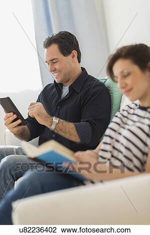 Stock Image - Couple sitting on sofa, man using digital tablet. Fotosearch