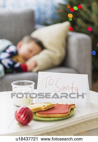 Stock Image - Gingerbread and glass of milk for Santa on foreground. Fotosearch