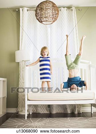 Stock Image - Girl (4-5) and boy (8-9) jumping on sofa. Fotosearch