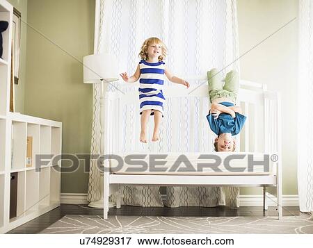 Girl (4-5) and boy (8-9) jumping on sofa View Large Photo Image Stock Photo - Girl (4-5) and boy (8-9) jumping on sofa. Fotosearch
