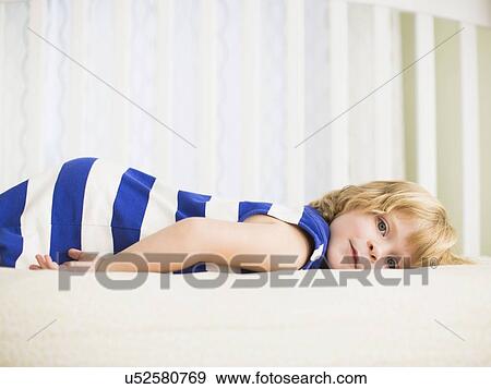 Stock Photo - Girl (4-5) resting on bed. Fotosearch
